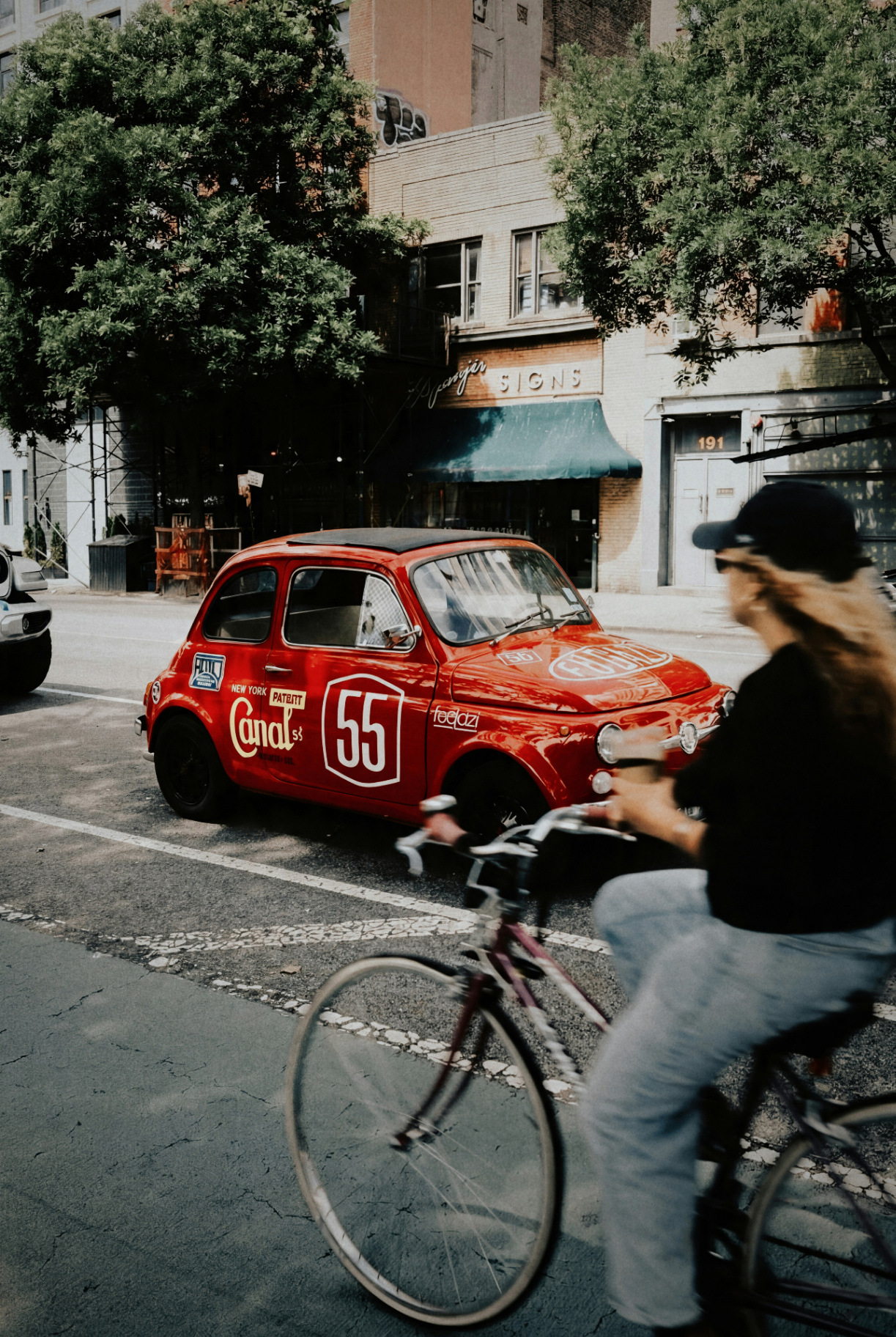 Cyclist passing a vintage red car on a city street